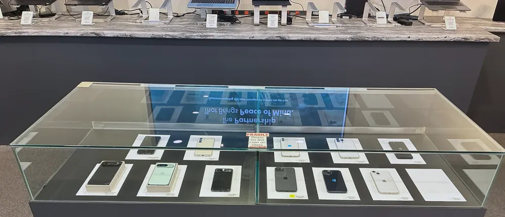 The glass cabinet in the middle of the outlet floor, holding boxed phones on printed cards, with laptops standing along the granite counter behind it.