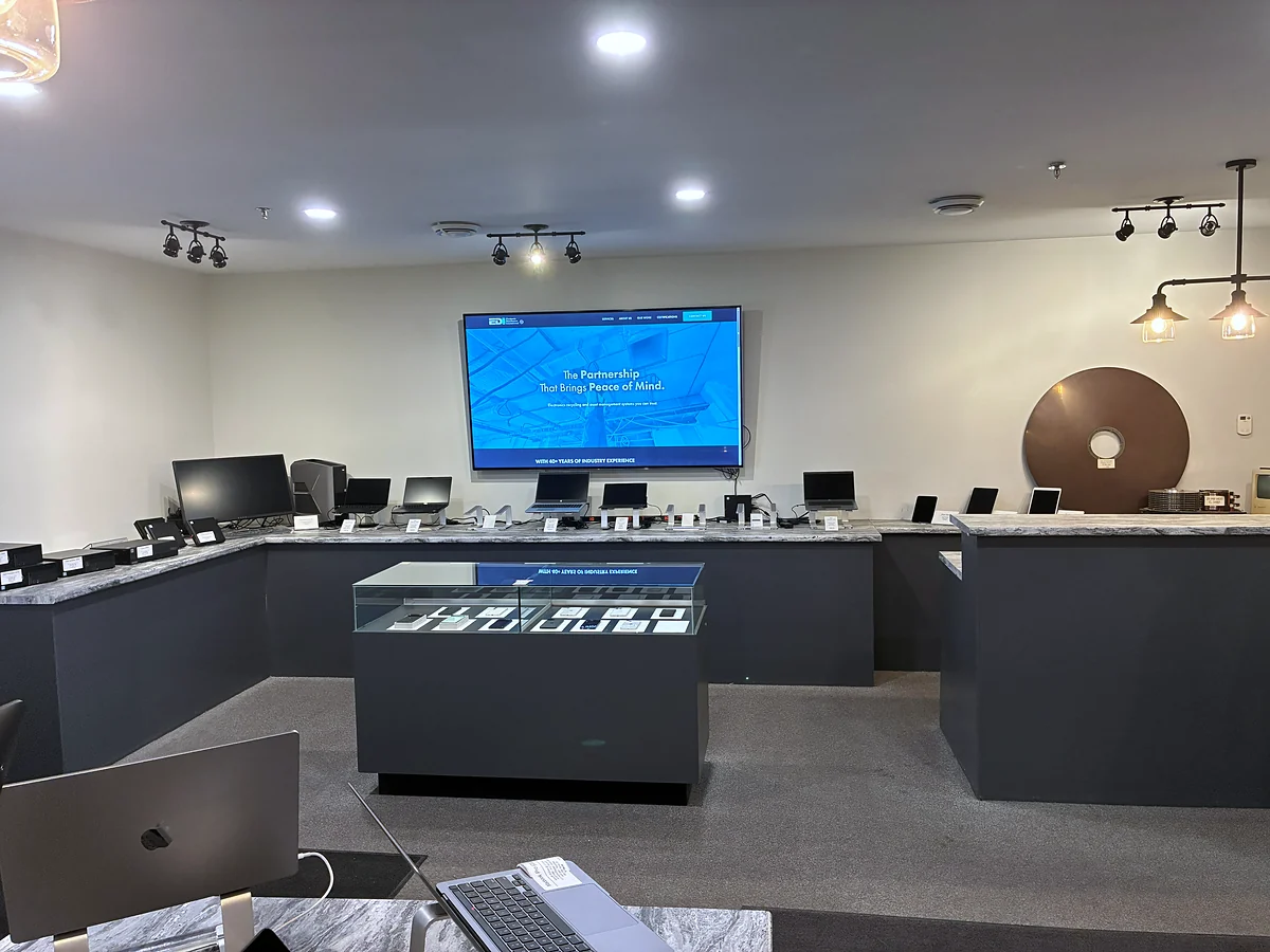 The counter inside the outlet at 35 Progress Drive. Laptops stand in a row along a granite counter, each on its own stand with a printed price card, and a glass cabinet of phones sits in the middle of the floor.